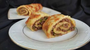 Fırından yeni çıkmış kıymalı rulo patates yemeği, üzerine erimiş kaşar peyniri eklenmiş.