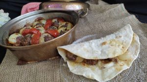 Pişmiş soğan kebabı, yanında közlenmiş domates ve biber ile servis ediliyor.