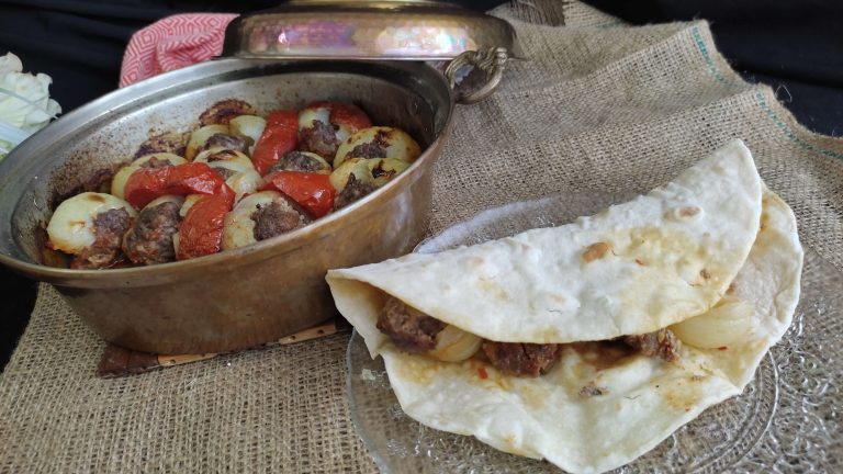 Pişmiş soğan kebabı, yanında közlenmiş domates ve biber ile servis ediliyor.