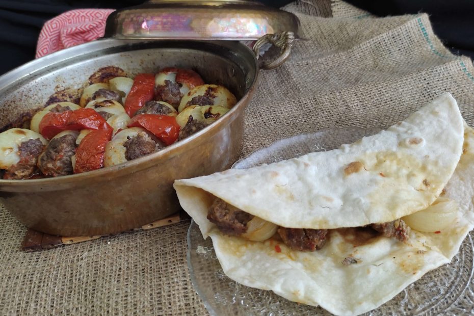 Pişmiş soğan kebabı, yanında közlenmiş domates ve biber ile servis ediliyor.